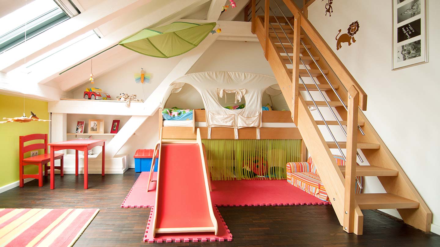 DachKomplett Lösungen und Leistungen rund um das Thema Dach. Hier ein helles Kinderzimmer mit Hochbett und Holztreppe in Speicherraum, Dachflächenfenster und Regallösung in offener Dachbalkenkonstruktion.